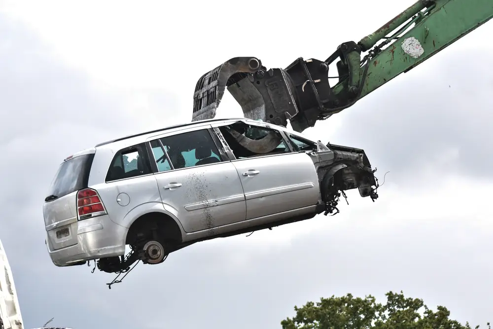 Car in a scrap yard being lifted by a mechanical grabber crane to be scrapped