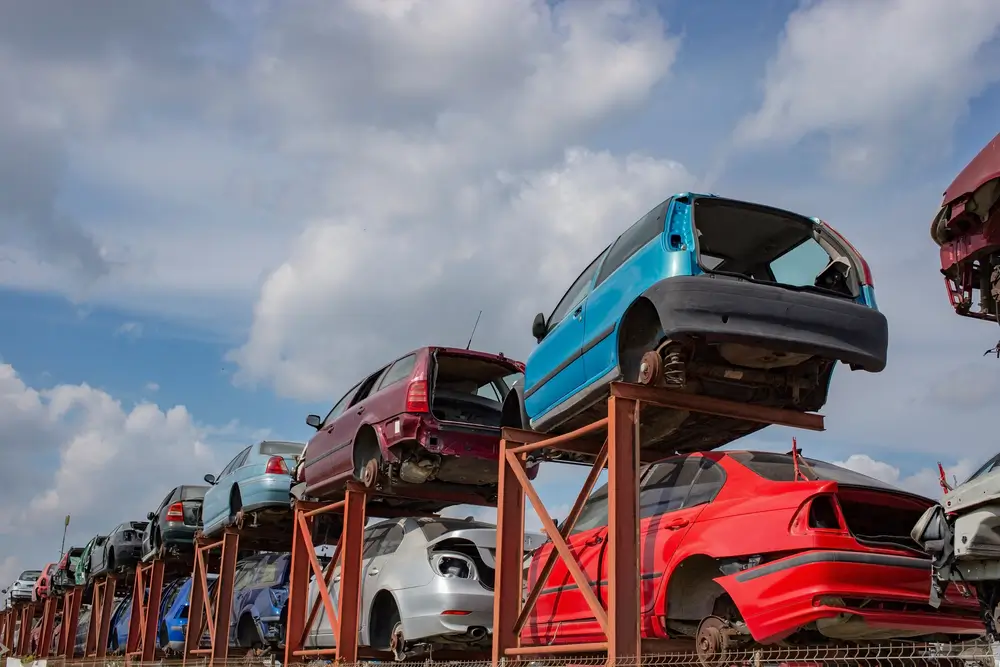 Stacked cars on a metallic frame, used for parts. Scrapyard perspective with blue skies and fluffy clouds. A lot of copy space